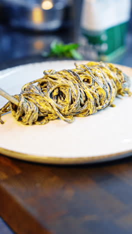pasta rolled on the tongs is laid on the large white plate. a piece of prawn is put on top. close up. vertical video.