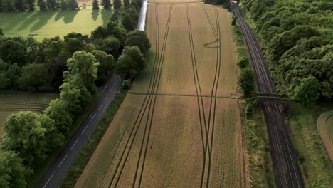 Vista-Aérea-De-Marcas-De-Tractores-En-Campos-Agrícolas-Entre-El-Ferrocarril-Y-La-Carretera