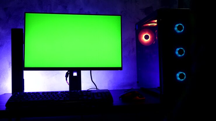 Computer desktop con schermo verde vuoto sul tavolo con luci LED RGB nella stanza buia.