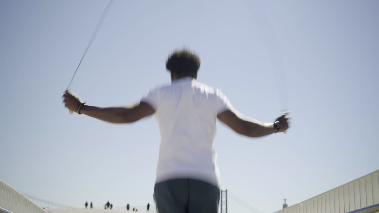 Rear view of African American sportsman skipping rope on bridge.