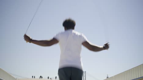 Rear-view-of-African-American-sportsman-skipping-rope-on-bridge.