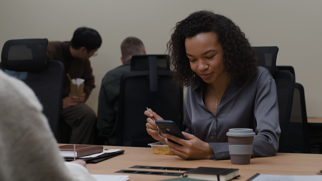 Woman using phone while eating lunch at office desk
