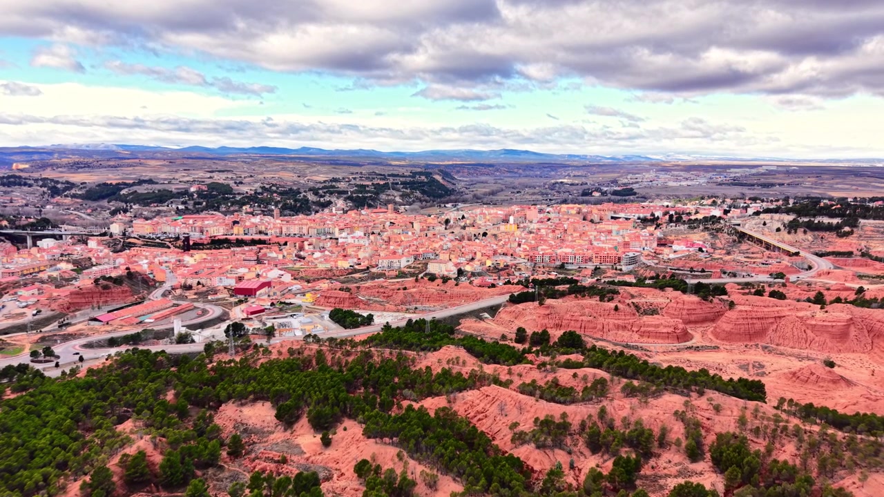 Paesaggio montano e città rossa, Teruel, Spagna. Vista aerea da drone di una foresta di pini, un canyon, un insediamento urbano storico e un cielo nuvoloso