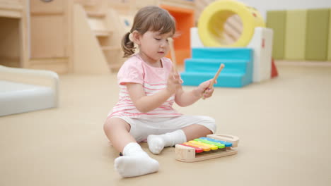 niña de 3 años tocando un instrumento musical de xilófono en la sala de juegos en cámara lenta, niño pequeño sentado en el flujo en el patio de recreo cubierto y golpeando con martillos en coloridas teclas de madera
