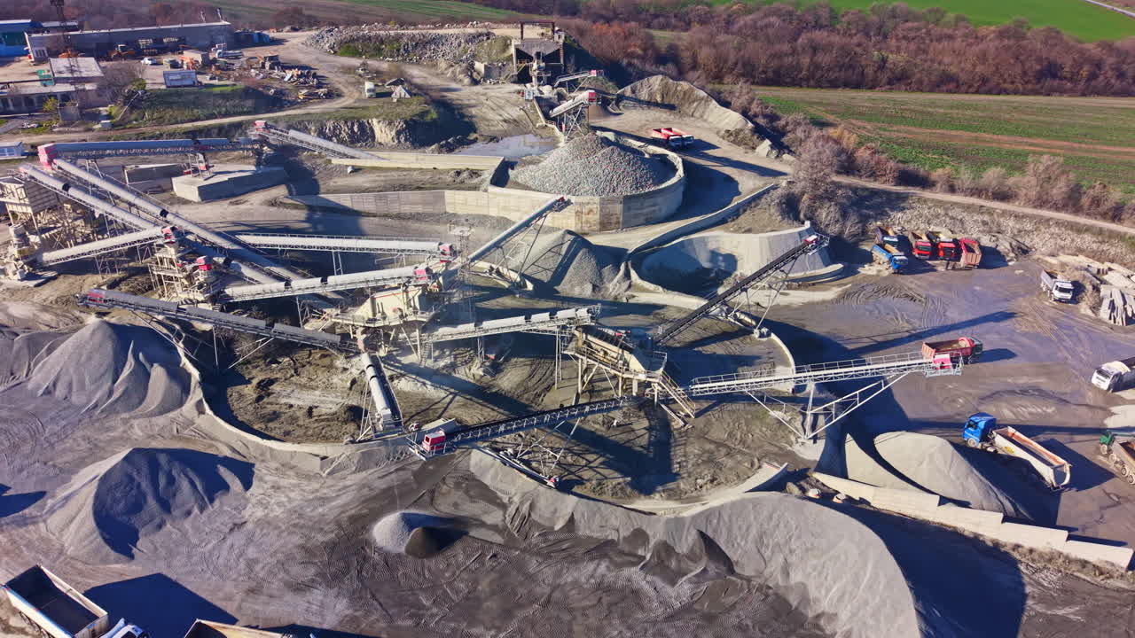 Vast industrial site showcasing gravel processing and transportation under bright sunlight with lush greenery in the background