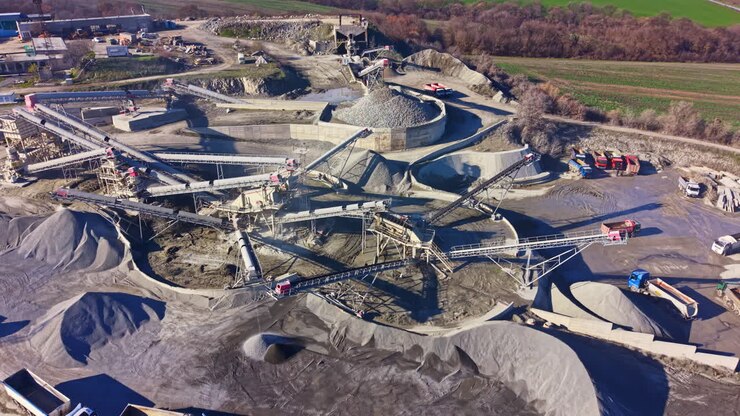 Vast industrial site showcasing gravel processing and transportation under bright sunlight with lush greenery in the background