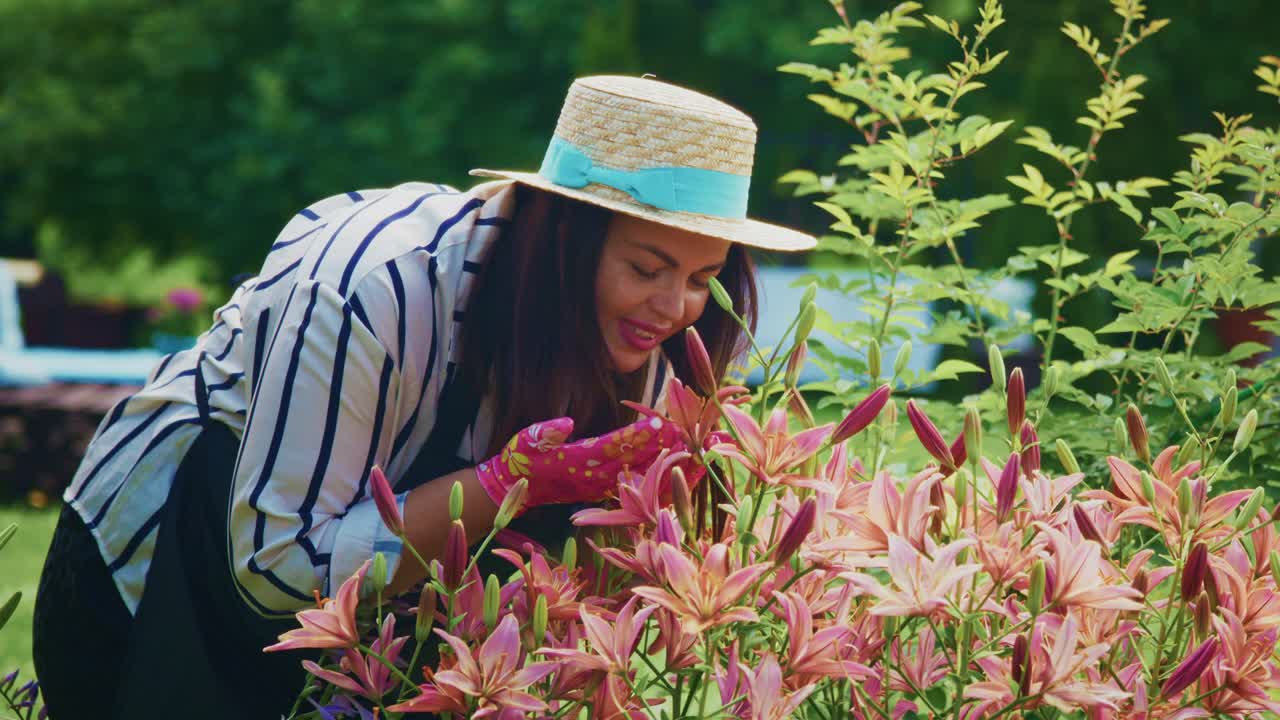 Woman in straw hat enjoying fragrant flowers in a vibrant garden during sunny day