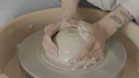 a female with tattoos working on the pottery wheel