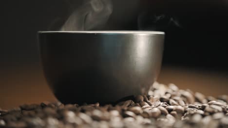 Steam-over-a-cup-of-coffee-on-a-wooden-table-surrounded-by-fresh-coffee-beans-slow-motion