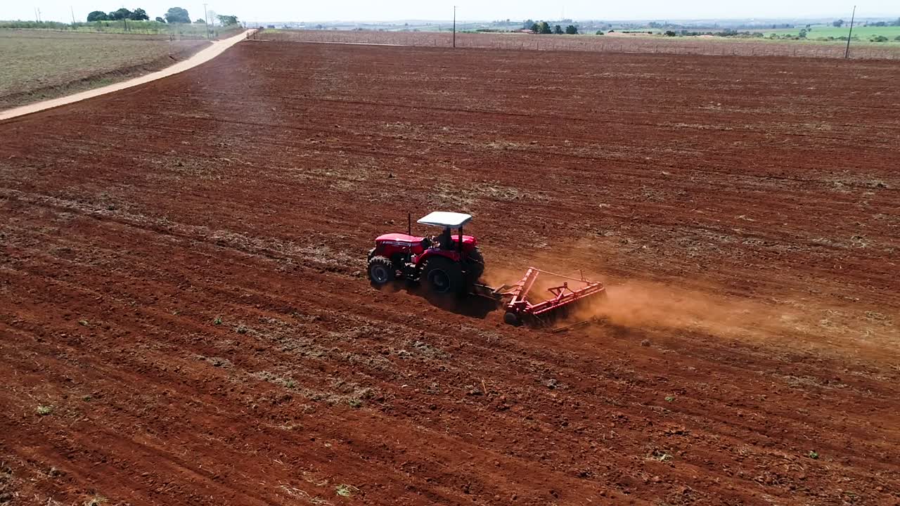 dron aéreo siguiendo por detrás y luego orbitando alrededor de un tractor preparando el suelo para la siembra de semillas y mostrando todo el campo