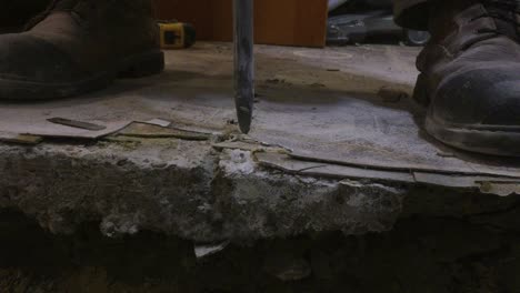 Medium-close-up-on-drill-bit-breaking-through-basement-concrete-floor,-creating-debris