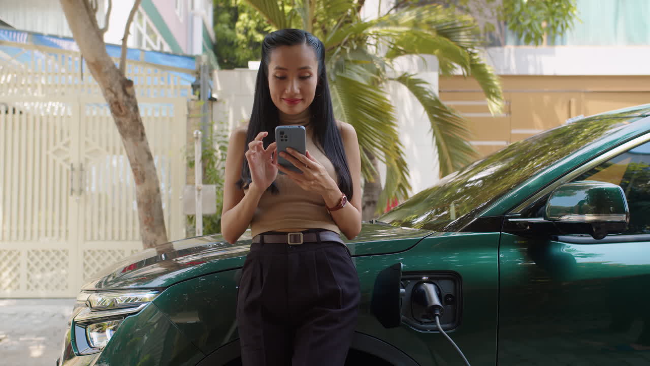 Woman using smartphone while charging her electric car