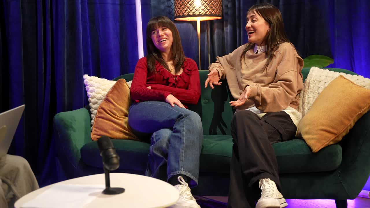 Two Young Women Talking and Laughing on a Green Couch