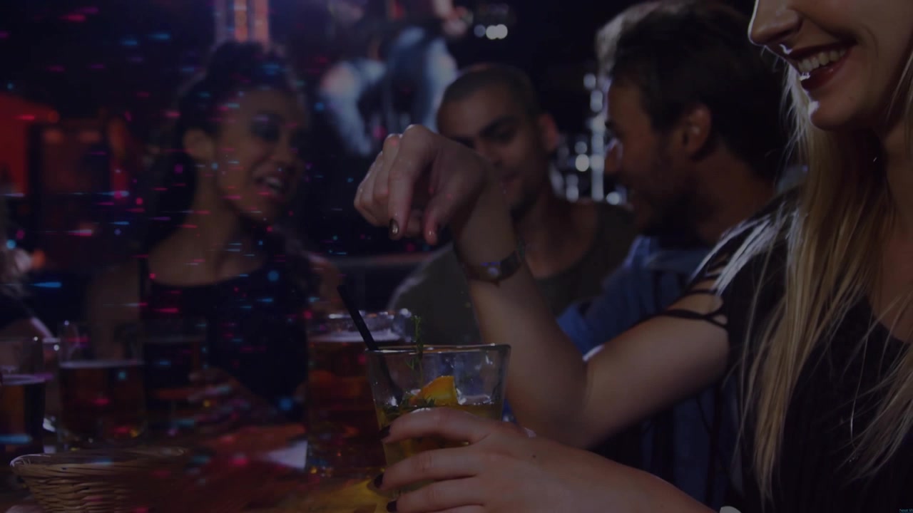 Donna bionda in canotta che prende un cocktail, posiziona una fetta di agrume e mescola la bevanda al bar, con spazio per il testo.