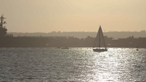 sailboat and aircraft carrier at sunset