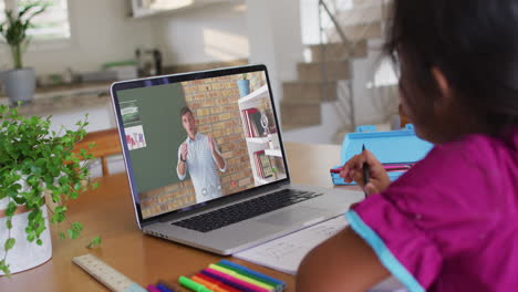chica biracial sentada en un escritorio usando una computadora portátil teniendo una lección escolar en línea