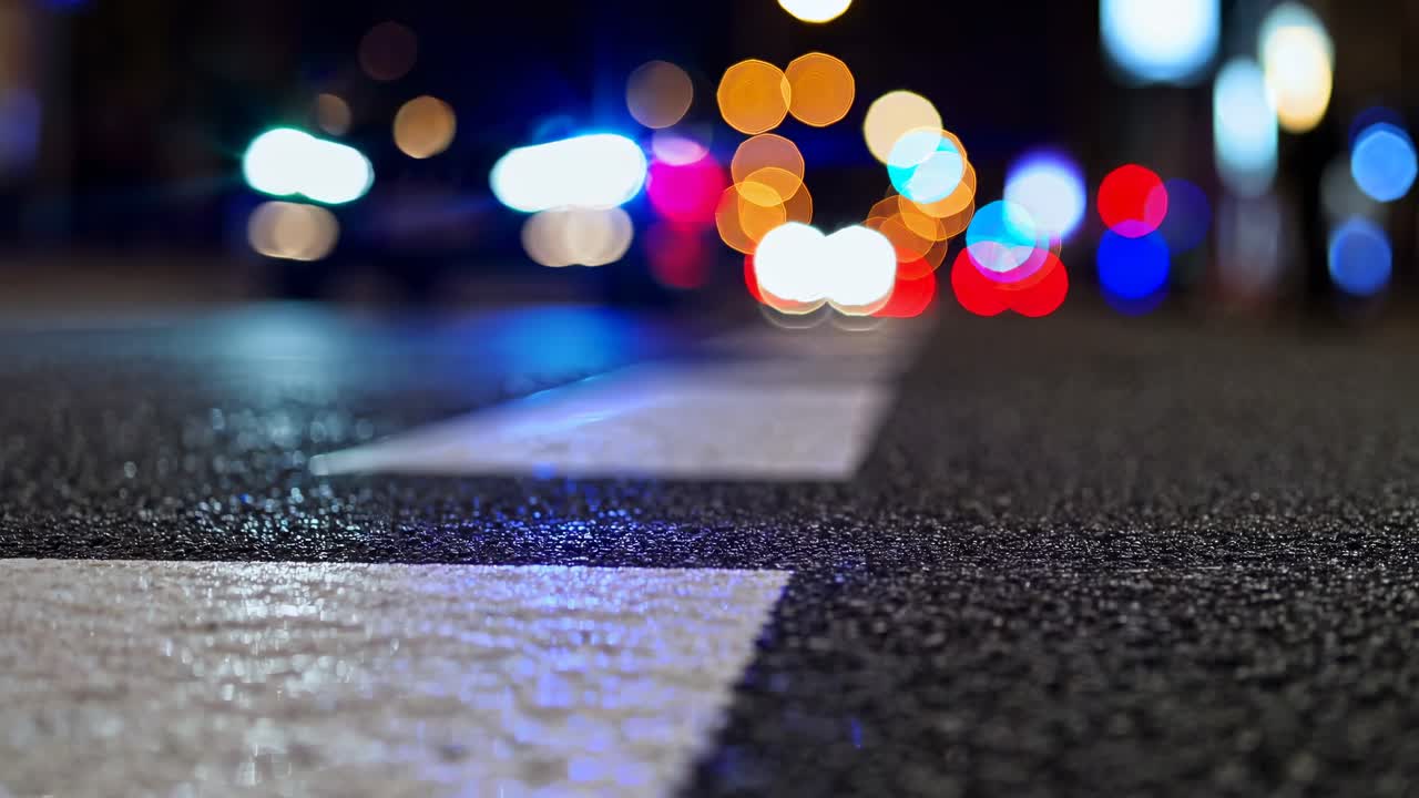 Blurred city streetlights at night with a low-angle focus on asphalt, creating a cinematic video