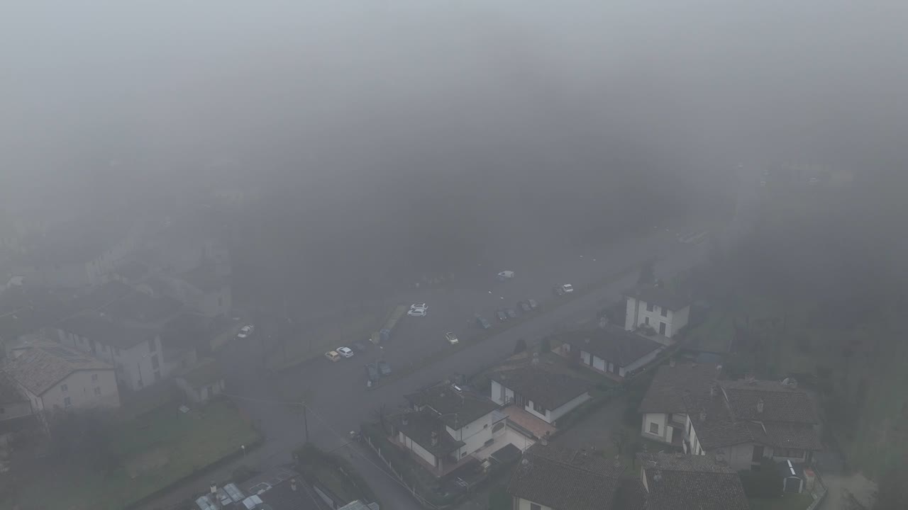 Aerial wide shot of Castell’Arquato in Emilia-Romagna, Italy, with medieval houses and streets barely visible through thick winter fog and low visibility atmospheric conditions