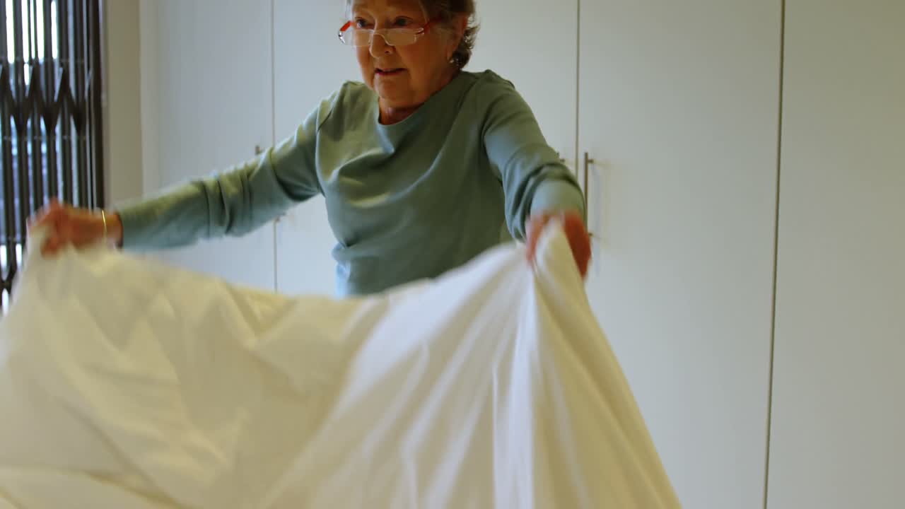 침실 4k에서 침대를 만드는 고령 여성