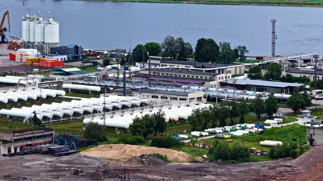 Gas depot with white storage tanks and pipelines near river at port site in Latvia
