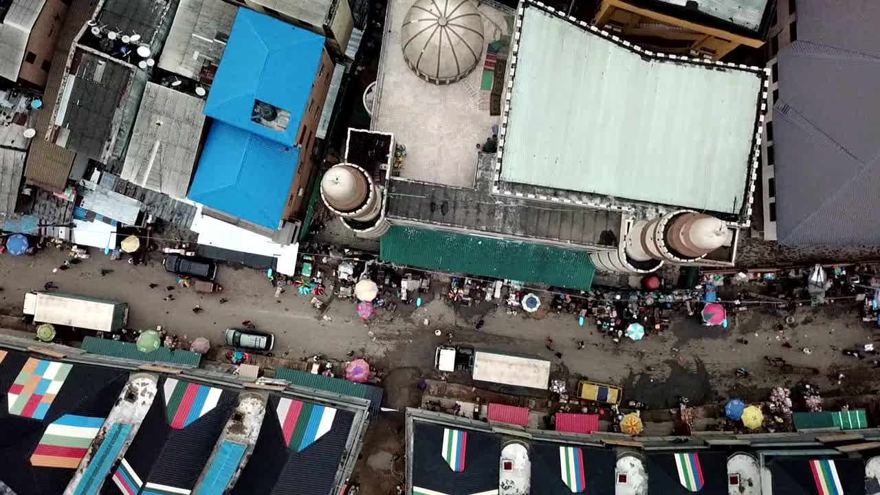 Veduta aerea zenitale con drone del mercato di strada di Lagos Island accanto alla Moschea Centrale di Lagos, Nigeria, con minareti, ombrelloni colorati e una strada affollata in un denso quartiere urbano.
