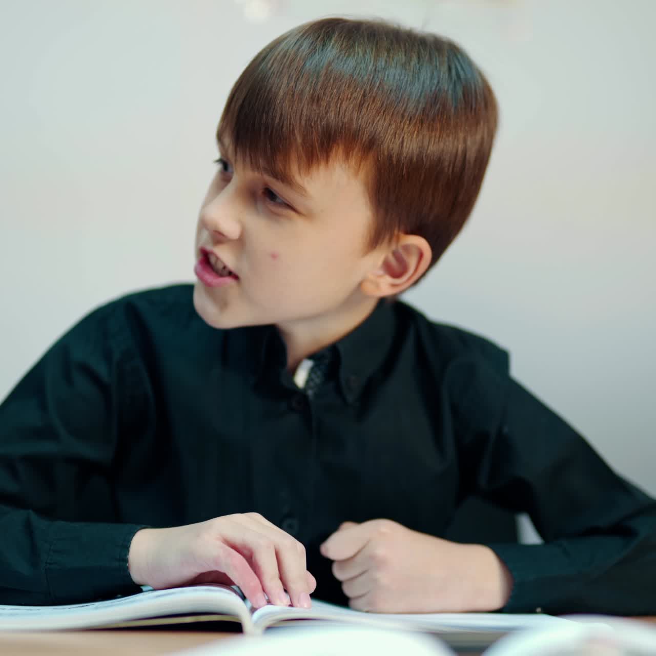 Cute boy in the classroom. Kid is sitting at the desk and listening to the teacher at primary school. Clever boy in black shirt talking during the lesson.