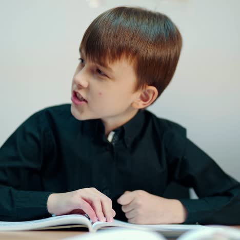 cute boy in the classroom. kid is sitting at the desk and listening to the teacher at primary school. clever boy in black shirt talking during the lesson.