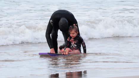 adult teaching child to surf on beach