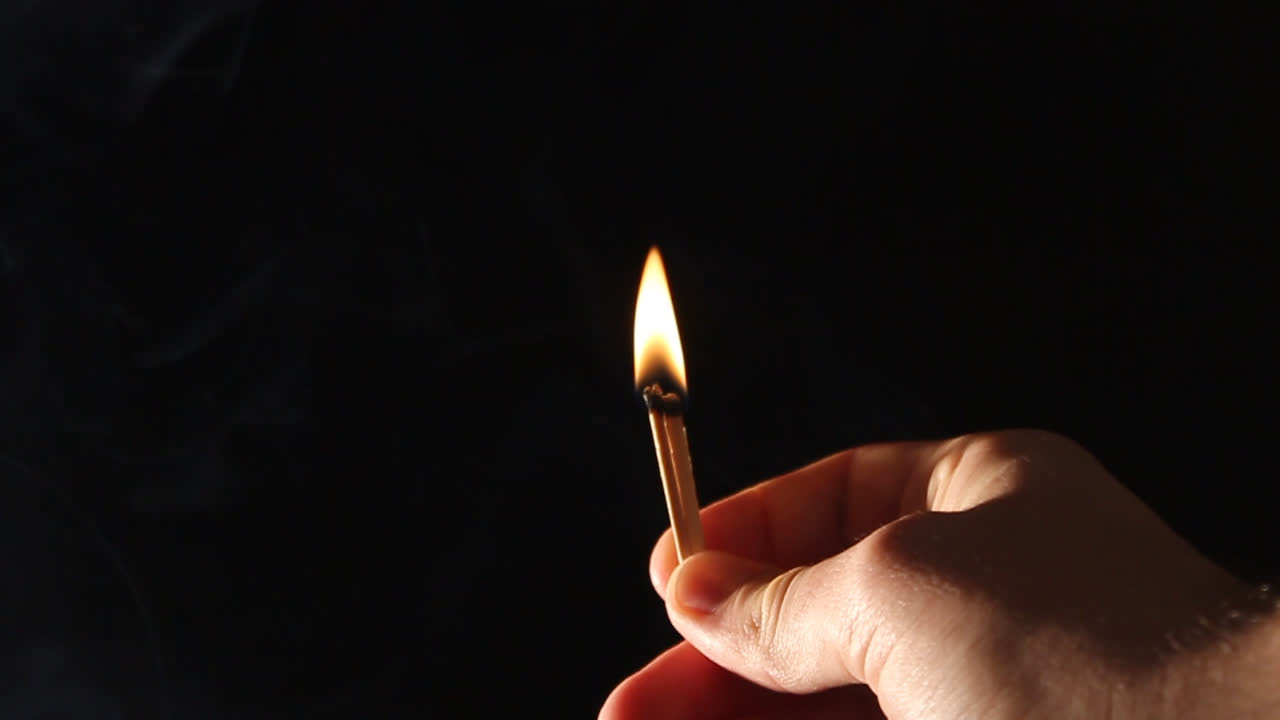 Hand Holding Burning Matchstick with Smoke on Black Background