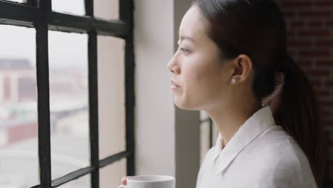 portrait beautiful asian woman drinking coffee at home smiling happy enjoying successful lifestyle looking out window planning ahead relaxing in cozy apartment loft