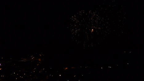 Celebration-with-colorful-and-sparkling-fireworks,-over-a-mountain-town,-at-night