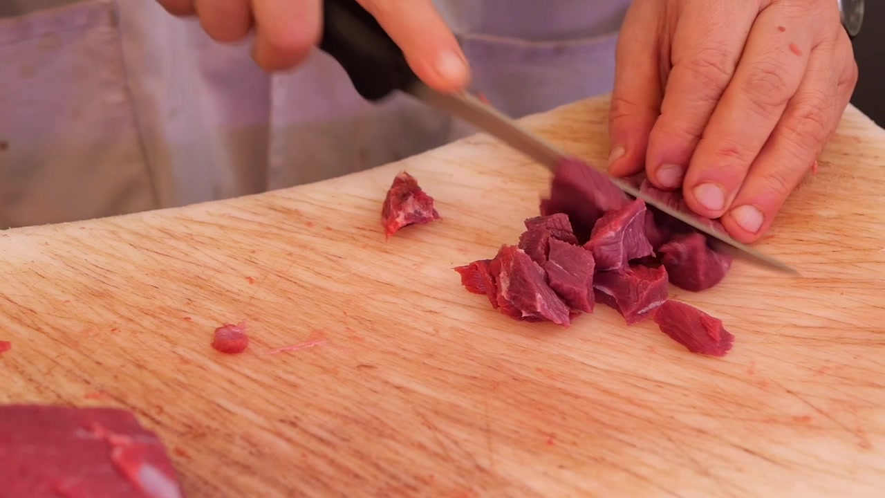 Butcher Cutting Fresh Raw Beef into Cubes on Wooden Board