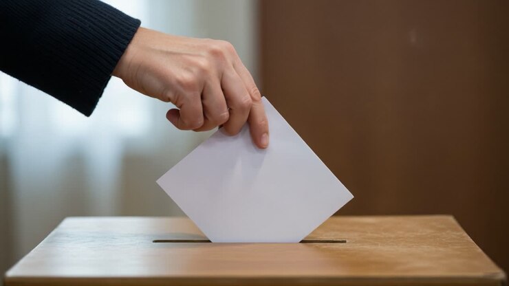 Esprimere un voto: Primo piano di una mano che inserisce una scheda elettorale in un'urna di legno, simboleggiando l'impegno civico e la partecipazione democratica nelle elezioni.