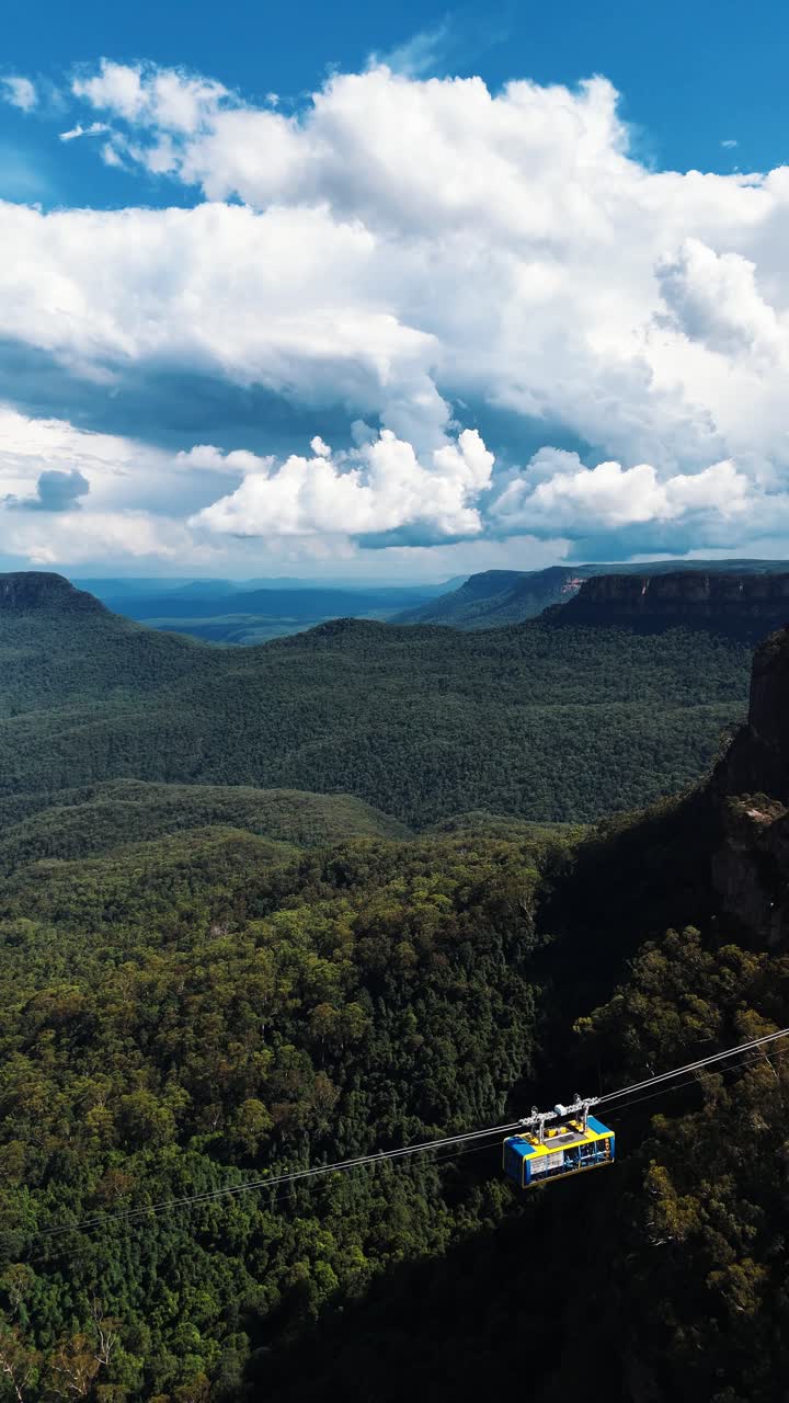 Vertical drone wide shot of gondola cable car at scenic world in blue mountains of Australia. Sunny with clouds and green forest landscape.