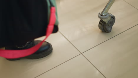 a close-up shot of a person wearing black boots, carrying a gym bag with red straps, and moving a shopping trolley in a mall. emphasizing the motion and casual nature of shopping or daily errands