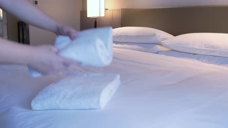 housekeeper is putting towel on the bed in the room