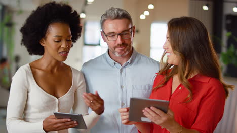 Multi-Cultural-Business-Team-With-Digital-Tablets-Meeting-In-Modern-Open-Plan-Office