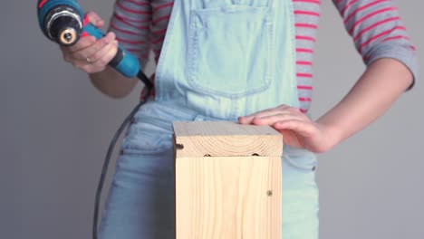 una mujer hace un trabajo no femenino - perfora un agujero con un destornillador en una caja de madera