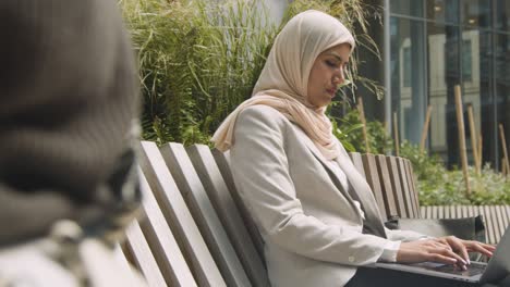 mujer de negocios musulmana sentada al aire libre en los jardines de la ciudad trabajando en una computadora portátil 2