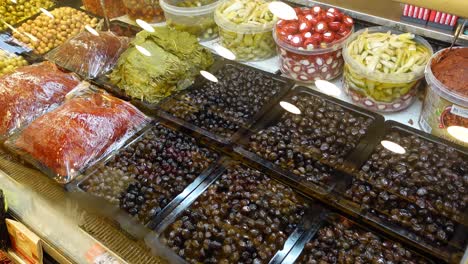 un primer plano de una exhibición de aceitunas, pepinillos y pimientos en un puesto de mercado