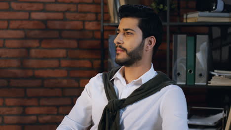 portrait of arabian businessman sitting in his office and looking at the side, then he turns his head to the camera and smiles