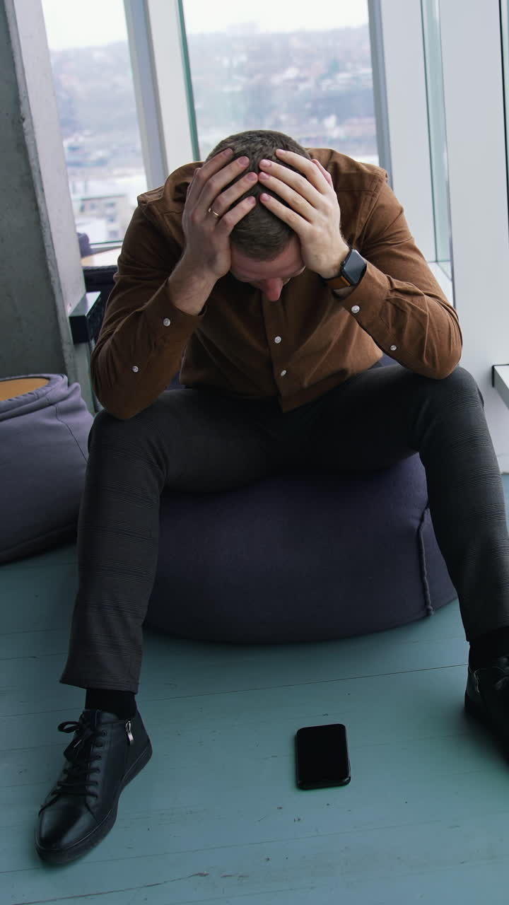 Businessman sitting in office by the large window. Thoughtful man with his hands on eyes becomes happy after finding the solution to the problem. Vertical video