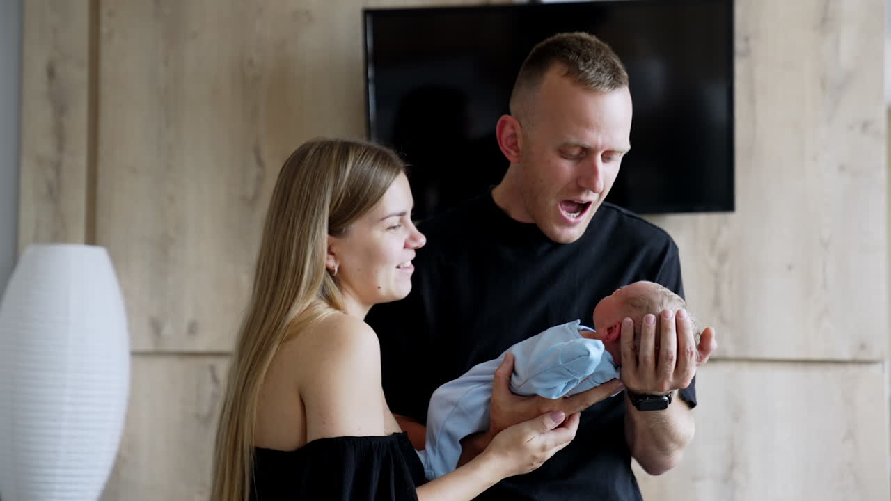 Happy couple looking at their newborn boy. Caucasian parents hold their baby talking to it.