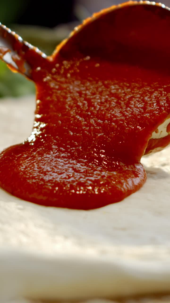 Pizza sauce being spooned onto pizza dough