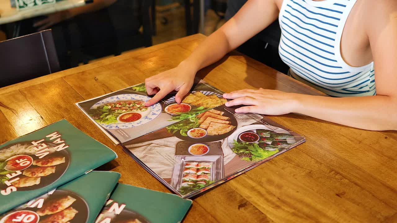 A person examines a Vietnamese restaurant menu in Bangkok, Thailand. Bright lighting highlights colorful dishes, creating an inviting atmosphere