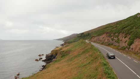 Forwards-tracking-of-car-driving-on-road-winding-above-sea-coast.-Meadows-and-pastures-in-slope-above-rocky-cliffs.-Ireland
