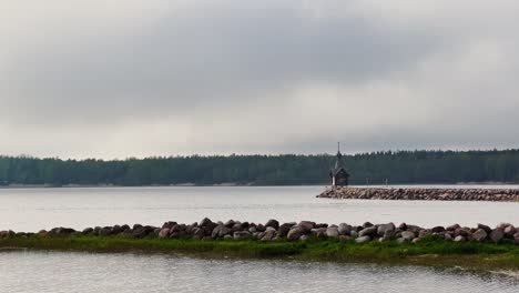 an old chapel stands on a stone promontory on the water in leningrad region russia at cloudy weather, the forest in the background