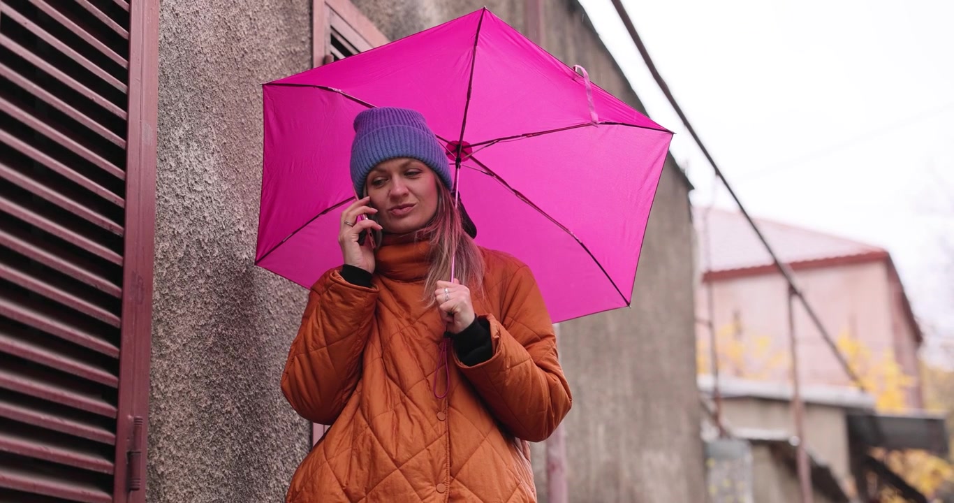 Giovane donna con ombrello rosa parla al telefono per strada