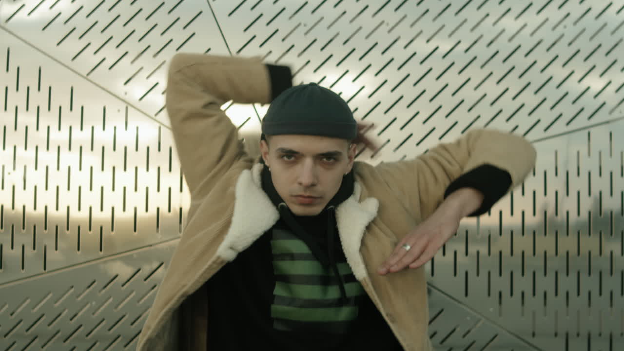 молодой человек в уличной одежде танцует вогу для камеры на открытом воздухе