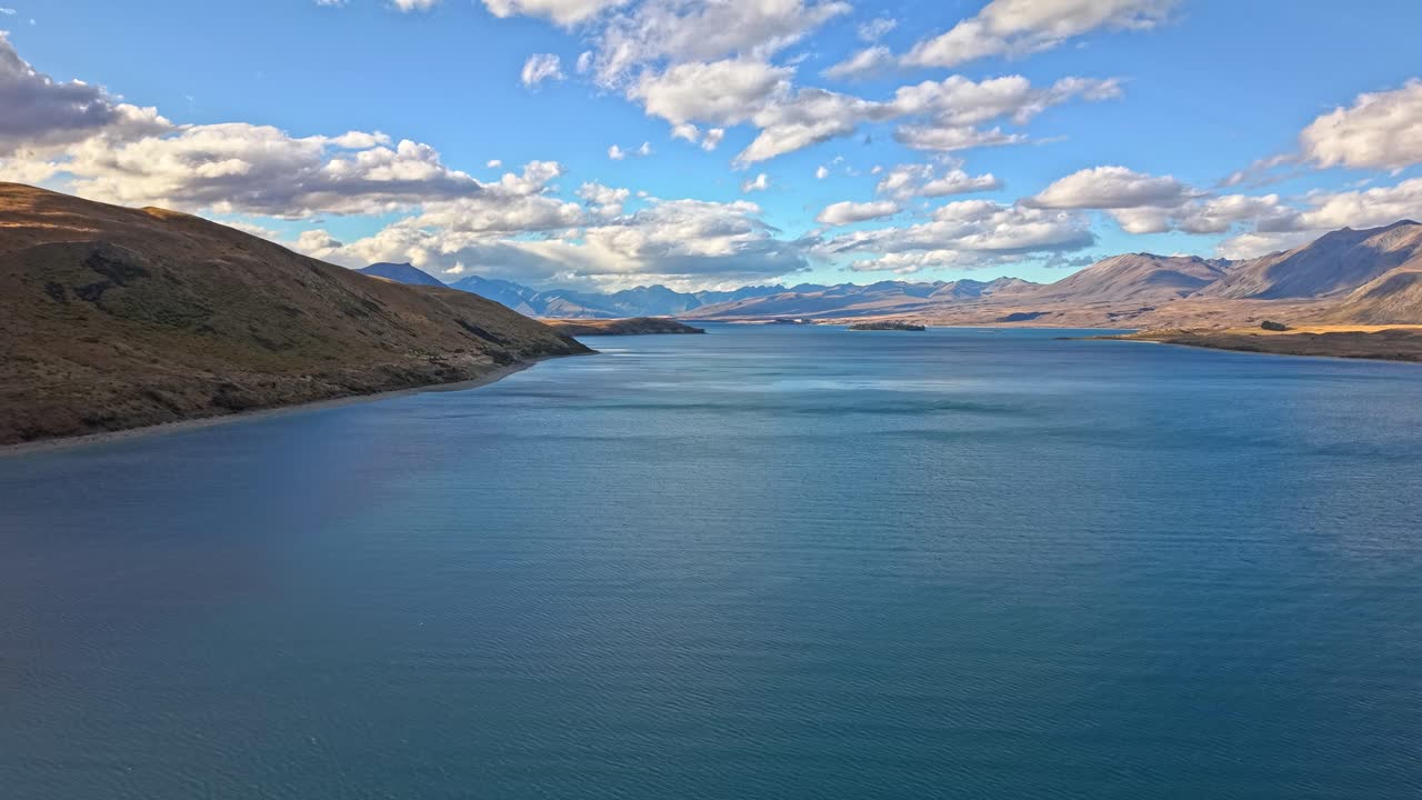 Blue lake in New Zealand with mountains, clouds, and clear sky